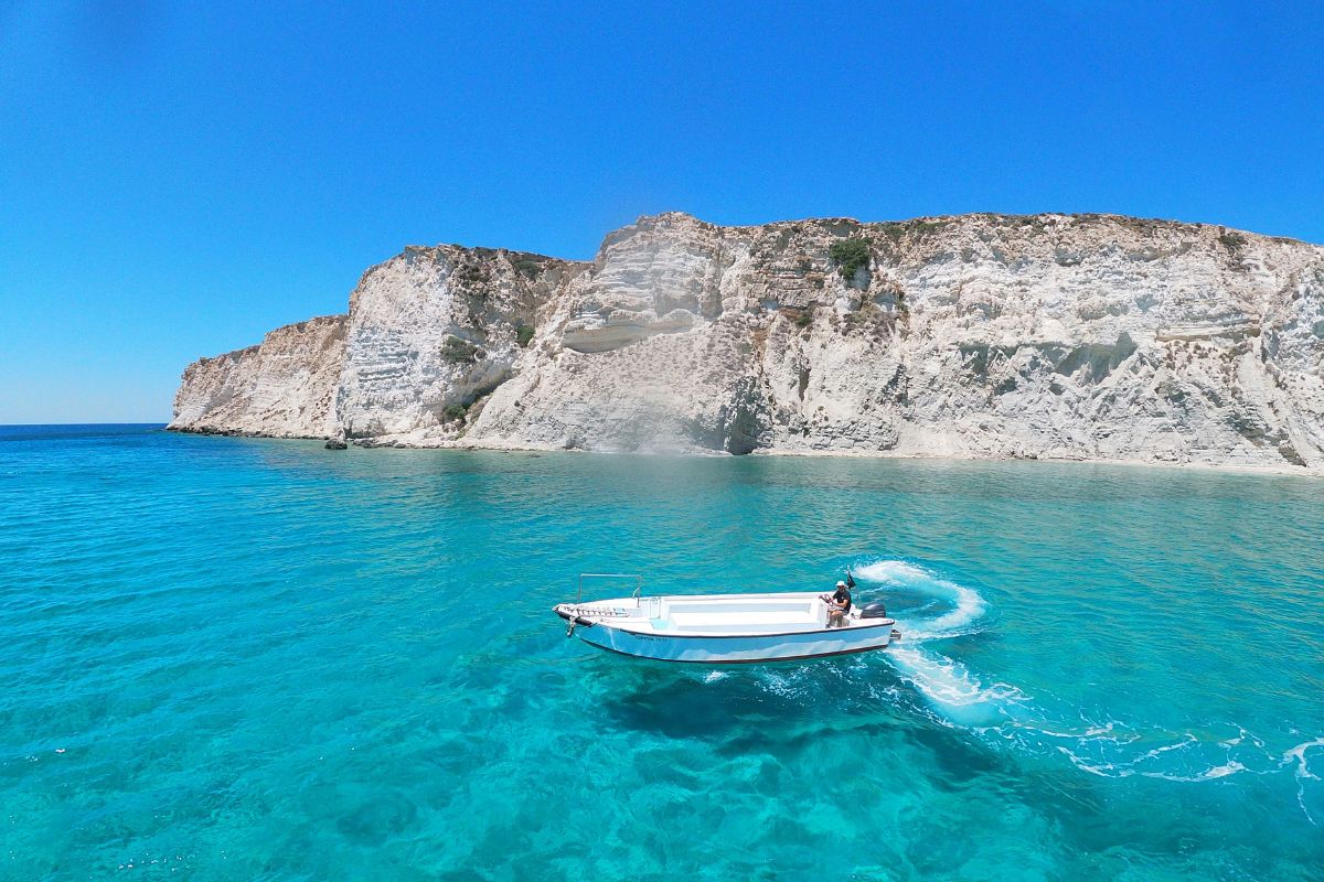 Boat tour along the Cretan coast in summer, with clear turquoise water and dramatic white cliffs under a bright blue sky.