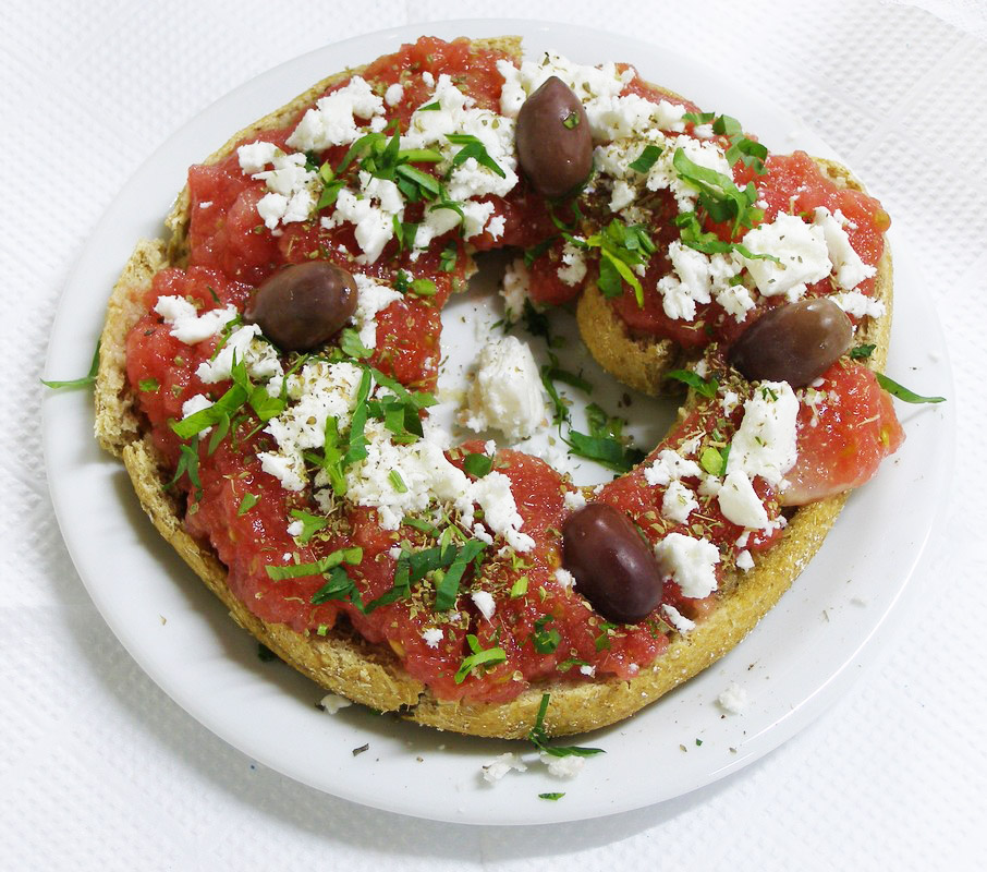 Cretan dakos with barley rusk, tomato, cheese, olive oil, oregano, and olives