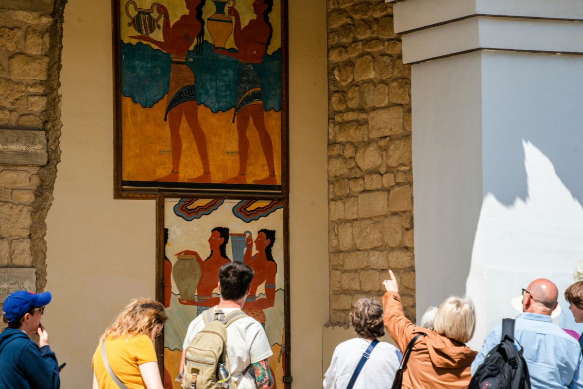Guided tour at Knossos Palace in Crete, with visitors viewing restored Minoan frescoes and ancient stone architecture.