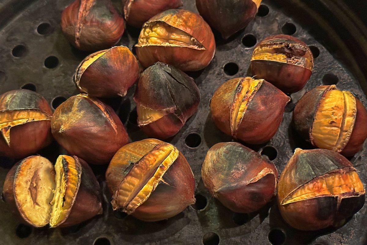Roasted chestnuts with cracked shells on a hot metal roasting pan.